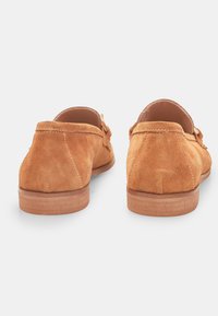 Suede loaferit vaaleanruskeana, joissa on sileä pinta, pyöreä takakappale ja yksinkertainen ompelu. Varustettu tasaisella puupohjalla.