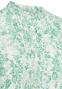 White fabric blouse with green floral print, featuring a band collar, pleats at the front, and button closure detail.