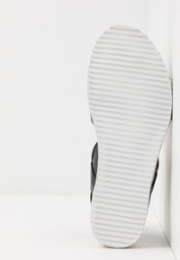 Chaussure noire avec une tige en cuir texturé et une semelle en caoutchouc blanc dotée de rainures horizontales pour l'adhérence. Design épuré et minimaliste.