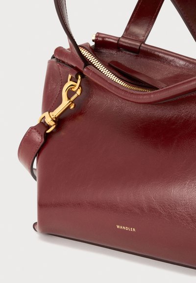 Sac à main en cuir rouge foncé avec fermeture éclair et boucle dorées, doubles poignées et petit logo doré "Wandler" sur le bas avant.