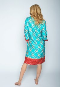 Turkusowy szlafrok w wzory z czerwonym geometrycznym wykończeniem, charakteryzujący się luźnym krojem i szerokimi rękawami. Gładki materiał o błyszczącym wykończeniu.