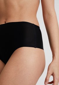 Black high-waisted underwear in a smooth, soft material with a seamless design. Features a short leg cut and minimal stitching details.