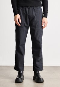 Calças cargo leves e pretas apresentam um corte descontraído, dois bolsos frontais e uma cintura elástica. Usadas com botas de tornozelo pretas.