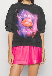 Sudadera gris oscuro con un gráfico de labios rojos y el texto "Lovers Kiss", con acentos en neón rosa y azul. Puños y cuello acanalados.