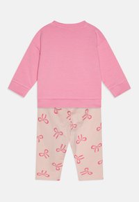 Rosa Baumwollpullover mit langen Ärmeln, kombiniert mit hellbeigen Leggings, die verstreute dunkelpinkfarbene Schleifenmuster aufweisen.
