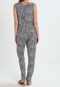 Czarny i biały kombinezon w wzory, bez rękawów, luźny krój z dopasowanymi kostkami, z okrągłym dekoltem i zapięciem na guziki z tyłu.