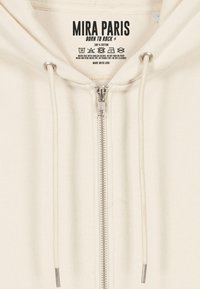 Felpa con zip beige in cotone, dotata di coulisse, con zip in metallo, texture a coste e etichetta stampata sul colletto.