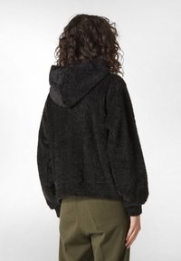 Felpa nera con cappuccio, morbida e dal taglio rilassato, con spalle scese e polsini a coste. Presenta un tessuto texturizzato e una tasca a marsupio.