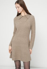 Kötött ruha világosbarna színben, bordázott textúrával, gallérral és hosszú ujjakkal, enyhén bővülő szegéllyel.