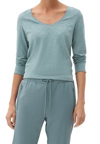 Hellblauer Langarmoberteil mit V-Ausschnitt, aus strukturiertem Stoff. Kombiniert mit passenden Jogginghosen mit Kordelzug und seitlichen Reißverschlüssen.