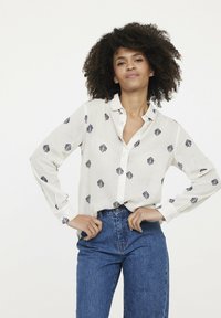 Chemise blanche à manches longues avec broderie florale colorée, col à boutons et poignets, assortie à un jean en denim bleu taille haute.