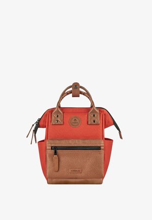 Kleiner roter und brauner Rucksack mit zwei Griffen, Reißverschlusstasche vorne, Seitentaschen und Cabaia-Logopatches auf der Vorderseite und am Griffverschluss oben.