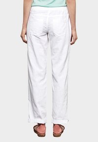 Pantalons en lin blancs au fit décontracté, avec deux poches arrière et des poignets retroussés, associés à des sandales à talons compensés marron.