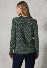 Chemise à manches longues de couleur vert foncé avec un motif en zigzag de vert clair. Fabriquée en tissu doux, elle dispose d'un col ras du cou et de manches ajustées.