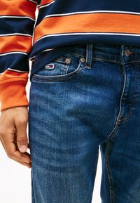 Käed kõrvuti, kannavad siniseid denimpükse ja pika varrukaga särki, millel on oranžid, mereväe- ja valged horisontaalsed triibud.