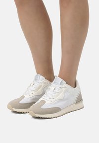 Sneaker con una combinazione di colori bianco e beige, realizzate con un mix di materiali in rete e camoscio, chiusura con lacci e suola testurizzata per una maggiore aderenza.