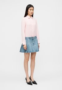 Ανοιχτό ροζ πουκάμισο με μακριά μανίκια, γιακά και κουμπιά μπροστά, συνδυασμένο με μπλε τζιν πλισέ φούστα. Μαύρες μυτερές γόβες ολοκληρώνουν το σύνολο.