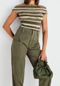 Top de punto a rayas en verde, marrón y crema; diseño off-the-shoulder. Pantalones cargo verde oliva con bolsillos de gran tamaño. Pequeño bolso de mano verde oliva.