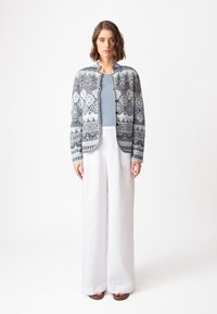 Adīta džemperis zilā un baltā krāsā ar ģeometriskām zīmējumiem, kombinēts ar gaiši zilu topu un baltām platām biksēm. Gluda tekstūra, ikdienas piegriezums.