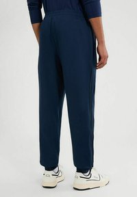 Marine joggers met een elastische tailleband, zijstrepen en taps toelopende enkelstukken, gecombineerd met witte sneakers met zwarte accenten en gelaagde sokken.