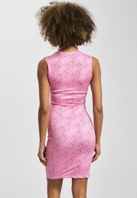 Różowa sukienka bodycon o błyszczącym wykończeniu, zdobiona powtarzającym się białym abstrakcyjnym wzorem, bez rękawów i dopasowanym kroju.