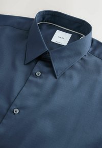 Granatowa koszula regular fit zapinana na guziki z opadającym kołnierzykiem oraz białą metką z napisem "NEXT" wewnątrz kołnierzyka.