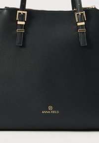 Čierna kabelka z textúrovanej kože s dvojitými remienkami a zlatými prackami, na prednej strane s malým zlatým logom Anna Field.