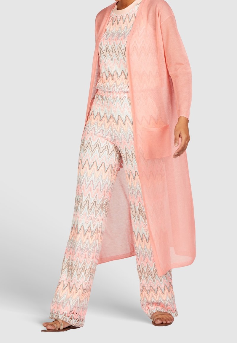 Lehký, průhledný korálový kardigan přes vzorovaný, zigzag pletený outfit v pastelových barvách, s kapsami a širokými, volnými kalhotami.