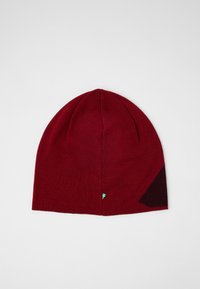 Gorro de punto rojo con forma redondeada y un patrón geométrico en un tono rojo oscuro en un lado. Presenta una pequeña etiqueta de logo en azul y amarillo.