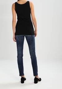 Top negro sin mangas combinado con jeans ajustados de color azul oscuro. Los jeans tienen un ligero desgaste y están estilizados con zapatos de tacón alto negros.