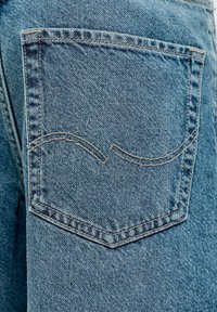 Zadné vrecko modrých riflí so dvojitým prešitým detailom zakrivenej švovej línie na tkanine.