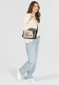 Borsa a tracolla nera e beige con un design floreale, materiale morbido, forma rettangolare, chiusura con cerniera e tracolla regolabile.