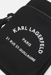 Czarna nylonowa torba na ramię z białym tekstem "KARL LAGERFELD," "PARIS" oraz adresem. Posiada zamek błyskawiczny i pleciony pasek.