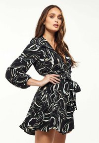 Black dress with wavy green and cream patterns, long sleeves, a v-neck, and a tied waist. Flared hem adds movement.