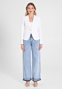Blazer blanc ajusté avec une fermeture à un bouton, associé à un jean large bleu clair avec un ourlet effiloché. Des talons dans des tons neutres complètent le look.