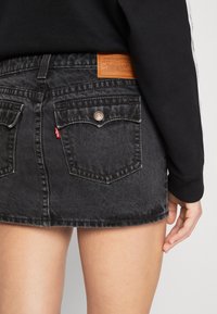Černá denimová mini sukně s dvěma zadními kapsami, s vybledlým vzhledem a koženou nášivkou na pase s detaily loga.