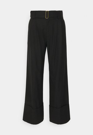 Pantalons larges noirs à taille haute, avec des plis devant et un détail de boucle rectangulaire en or sur la ceinture. Tissu au toucher lisse.