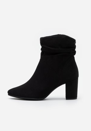 Bottine noire en daim souple, dotée d'une tige relâchée, d'un bout pointu et d'un talon épais. Design simple sans éléments métalliques apparents.