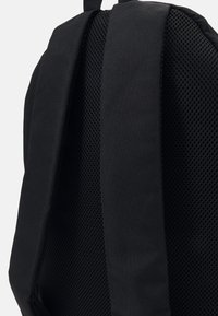 Mochila negra con correas de malla texturizada y acolchada, y un cuerpo de tela suave. El diseño enfatiza la comodidad y durabilidad para el uso diario.