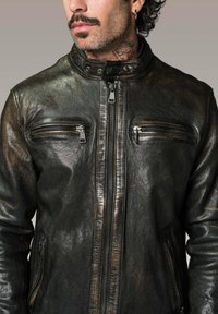 Veste en cuir noir avec une texture légèrement usée, dotée d'un col haut, d'une fermeture éclair à l'avant et de deux poches zippées sur la poitrine.