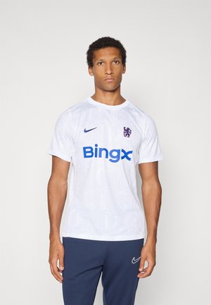 Bijela Nike nogometna majica s plavim "Bingx" logotipom, grbom kluba i suptilnom teksturom slova. Uparena s tamnoplavo hlačama.