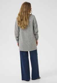 Grauer Strickpullover mit langen Ärmeln, kombiniert mit weit geschnittenen dunkelblauen Jeans, die Verzierungen entlang der Seitennaht aufweisen.