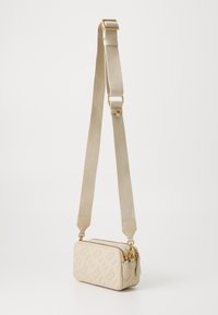Beige schoudertas met reliëflogo, gouden hardware en een textuurstofriem. Rechthoekige vorm met ritssluiting.