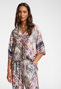 Mehrfarbige Seidenbluse mit Kapuze, die ein abstraktes Muster aus Blau, Pink und Creme aufweist. Lockere Passform mit kurzen Ärmeln.