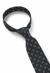 Zwarte stropdas met een herhalend wit bloemmotief, gemaakt van gladde stof met een elegante textuur, ontworpen in een traditionele smalle vorm.