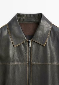 Dark green leather jacket with a prominent collar, zip closure, and contrasting stitching. Smooth texture with a minimalistic design.