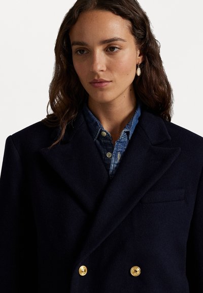 Marineblaue Wolle Doppelreiherjacke mit goldenen Knöpfen. Innenshirt aus Denim mit spitzem Kragen. Glatte Textur, taillierte Passform und klare Linien.