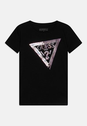 Melna organiskā kokvilnas T-krekli, kurā ir trīsstūrveida sudraba un varavīksnkrāsas rhinestone grafika ar "GUESS U.S.A." tekstu un abstraktu dizainu.