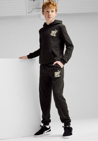 Sudadera negra con bolsillo frontal y logo, combinada con joggers a juego que tienen un bolsillo lateral. Hecho de una tela suave y texturizada. Zapatillas negras.
