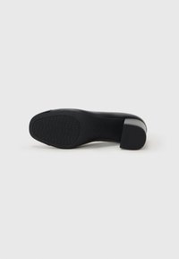 Scarpa nera con tacco alto, caratterizzata da una tomaia liscia, un tacco spesso e una suola in gomma testurizzata con un motivo geometrico per una miglior aderenza.